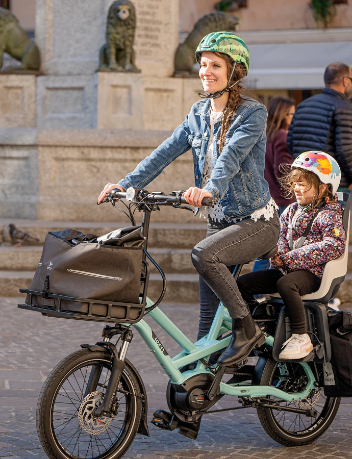 Une maman sur un vélo avec des courses à l'avant et un enfant derrière, tern GSD